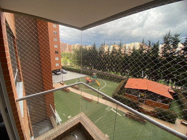 Balcon en vidrio con malla de seguridad y vista a un parque infantil