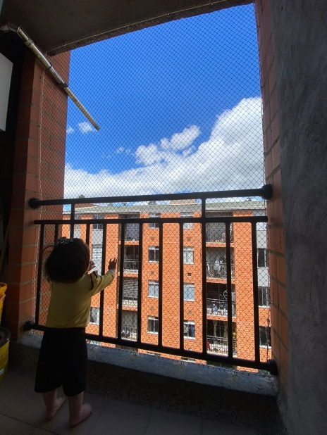 Niño pequeño apoyado en la baranda de un balcón protegido con malla de seguridad