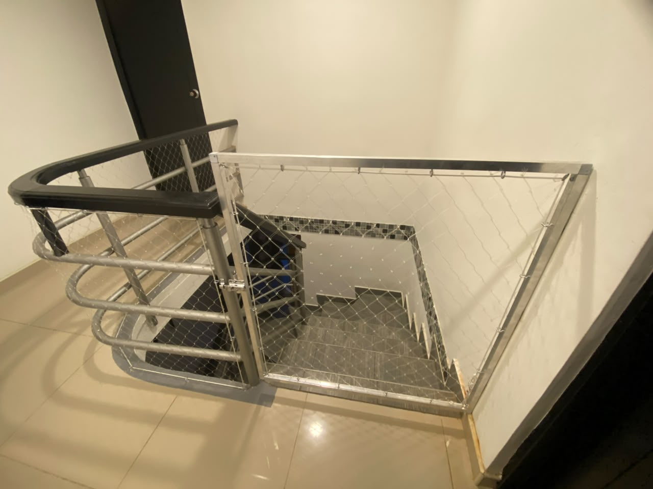 Hueco de escaleras cerrado con malla de seguridad y puerta abatible